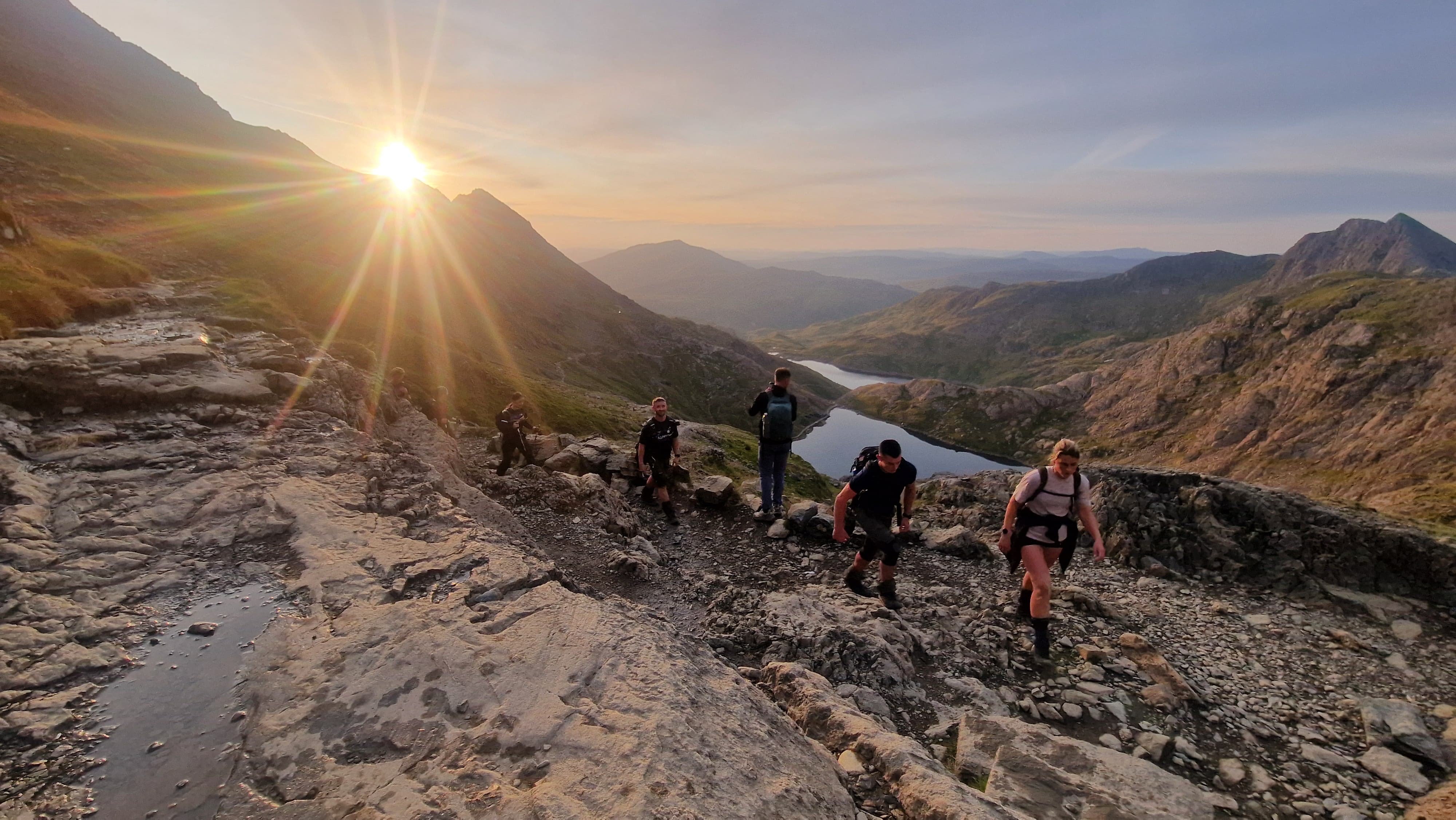 Climbers ascending a mountain trail toward the sunrise on the National Three Peaks Challenge